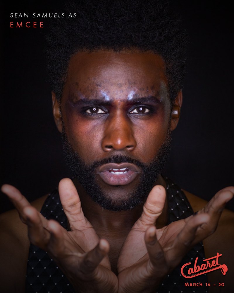Cabaret character portrait: Sean Samuels as the Emcee, glitter brow, hands reaching toward the camera