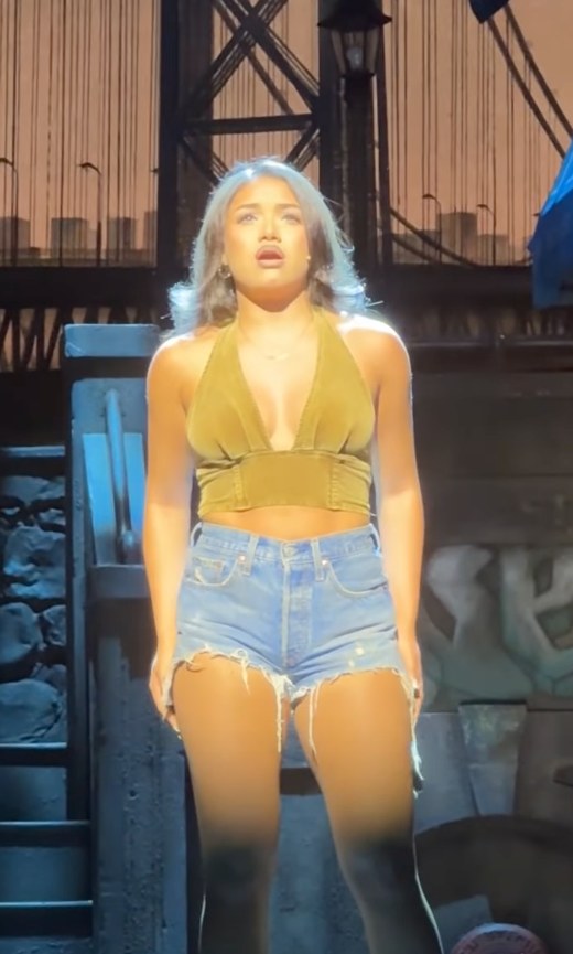 In the Heights reel: a performer alone in a spotlight mid-song, the George Washington Bridge behind her
