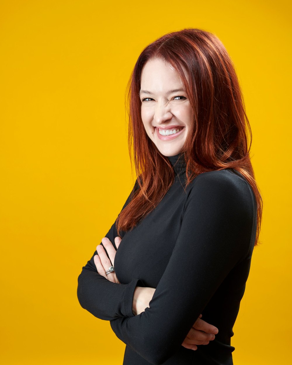 Lindsey May grinning with arms crossed against a golden yellow backdrop
